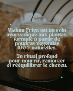 Gros plan, légèrement en plongée, sur un pot en verre transparent, centré, rempli d'une poudre fine brun clair et coiffé d'un couvercle en verre assorti. Le texte principal, en caractères élégants vert menthe, est superposé sur l'image et lit : 'Vishnu Priya est un soin ayurvédique aux plantes, formulé à partir de poudres végétales 100 % naturelles. Un rituel profond pour nourrir, renforcer et rééquilibrer le cheveu.' En arrière-plan flou, des nuances de brun clair évoquent des textures naturelles comme de l'osier ou du bois. Deux petites étoiles scintillantes blanches ajoutent une touche d'éclat au texte, en haut à gauche et en bas à droite.