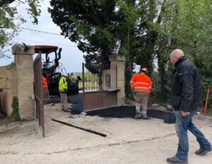 Ouvriers appliquant de l'enrobé noir avec un finisseur pour rénover une allée d'entrée de propriété, sous la surveillance d'un homme.